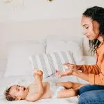 femme jouant avec bébé sur le lit, couches et jouets pour nourrisson