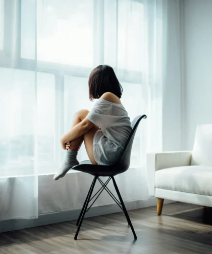 femme assise près d'une fenêtre, regard pensif, illustrant la dépression parentale